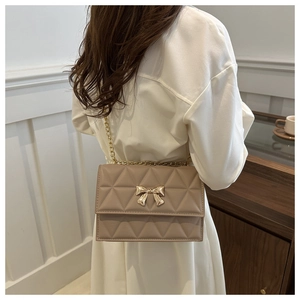 Detail of a beige quilted crossbody bag with a gold bow clasp on a female model