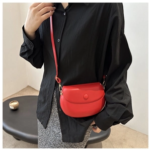 Detail of red saddle bag with gold metal hardware and adjustable shoulder strap on a model