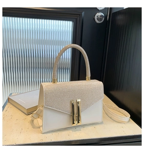 Close-up of cream square handbag with glitter flap texture and gold metal lock detail