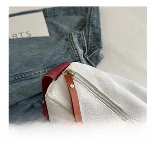 Detail of white canvas bag with brown leather zipper pull and burgundy shoulder strap