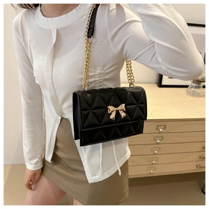 Detail of black quilted shoulder bag with golden bow clasp and metal chain strap