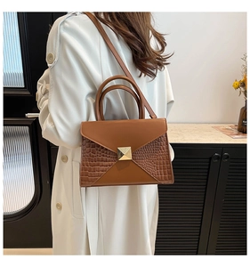 Detail of caramel brown handbag with crocodile texture side panels and gold square buckle
