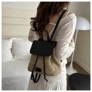 Detail of woven straw backpack with black leather straps on model in a minimalist room