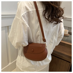 Sacoche selle en cuir marron portée à l'épaule sur un fond d'intérieur épuré