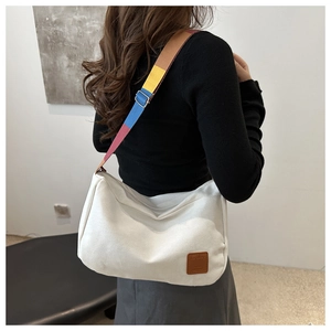 Detail of white canvas tote bag with multi-color striped strap and brown leather patch