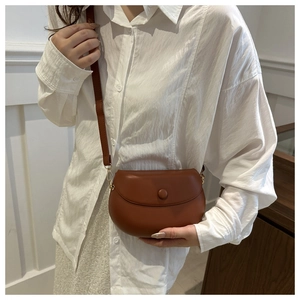 Sac besace marron porté à l'épaule, avec boucle circulaire et finition en similicuir lisse