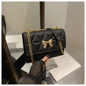 Detail of a black quilted shoulder bag with a gold metal bow clasp and chain strap