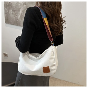Model wearing a white canvas tote bag with a colorful striped strap and leather patch