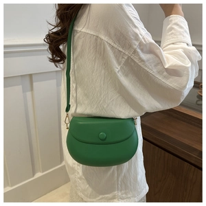 Détail du sac besace en cuir vert porté en bandoulière avec finitions dorées chic