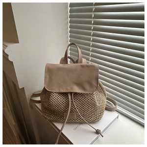 Detail of a beige woven backpack with leather flap and drawstring closure in sunlight