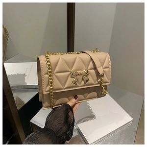 Close-up of beige quilted crossbody bag with a delicate golden metal bow detail