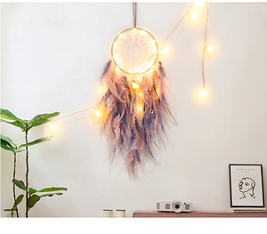 Close-up of pink dreamcatcher with glowing LED lights and delicate feathers on white wall