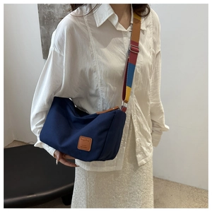 Detail of navy canvas crossbody bag with a colorful striped strap and leather logo patch