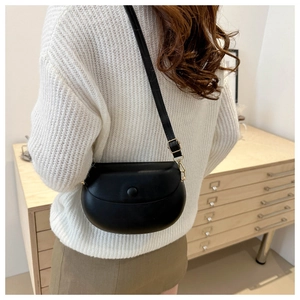 Detail view of a black saddle crossbody bag worn by a model in a minimalist indoor setting