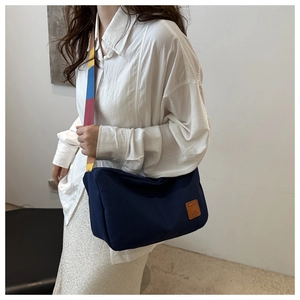 Detail of navy canvas crossbody bag featuring a colorful striped strap and leather patch