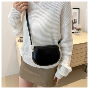Detail of minimalist black semi-circle saddle bag with glossy finish and snap closure