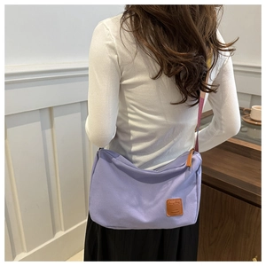 Detail of lavender canvas crossbody bag with colorful woven strap and brown leather logo