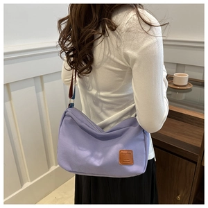 Close-up of light purple canvas crossbody bag with contrast shoulder strap and leather patch