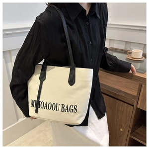 Minimalist cream canvas tote bag with black leather handles shown on shoulder