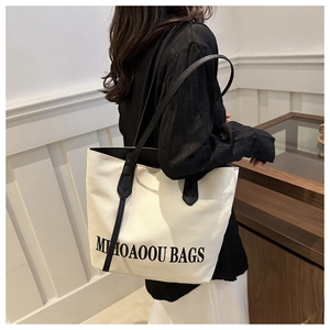Close-up of cream canvas tote bag with black straps and MIHOAOOU BAGS text on model