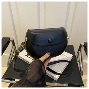 Detail of a minimalist black leather saddle bag with gold metal buckle and hand strap