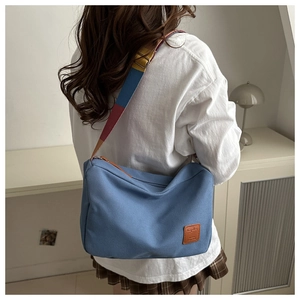 Close-up of blue canvas tote bag featuring a colorful striped woven shoulder strap