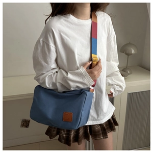 Close-up of blue canvas crossbody bag with colorful rainbow strap and leather logo detail