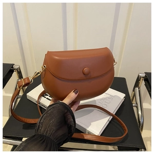 Detail view of caramel brown leather saddle bag with round flap buckle and gold hardware