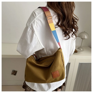 Detail of mustard yellow canvas bag showing colorful striped wide shoulder strap and side label