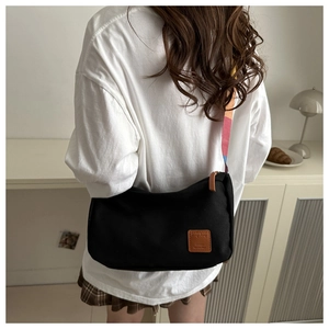 Detail of black canvas shoulder bag featuring a vibrant multi-color striped wide strap