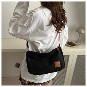 Detail of black canvas crossbody bag with leather logo tag and striped strap