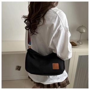 Detail showing the striped wide shoulder strap and leather patch on the black tote bag