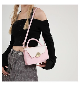 Detailed view of pink and beige crossbody bag with golden buckle on a fashion model