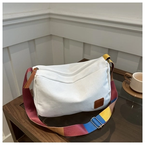 Detail of white canvas tote bag featuring a multi-color striped wide shoulder strap and leather patch