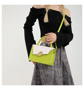 Detail of green and beige leather handbag featuring a golden oval metal lock and strap