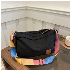 Detail of black canvas crossbody bag featuring a vibrant multi-color wide woven strap