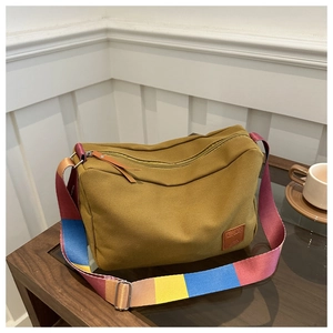 Detail of mustard yellow canvas tote bag featuring colorful striped strap on wooden table