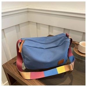 Close-up of blue canvas tote bag with a colorful striped strap on a wooden table