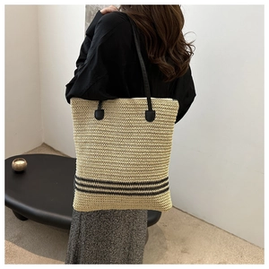 Detail of minimalist straw tote bag with black stripes and shoulder straps on a model
