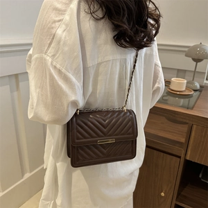 Quilted dark brown crossbody bag with gold chain strap worn with a white shirt