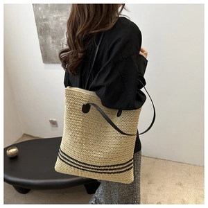 Detail of handwoven straw tote bag featuring black striped accents and slim straps