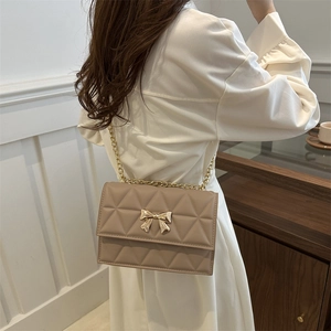 Khaki quilted crossbody bag with a gold bow buckle and chain strap shown on model