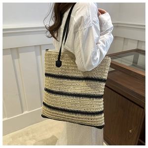 Detail of woven straw tote bag with black stripes worn by model in a minimalist room