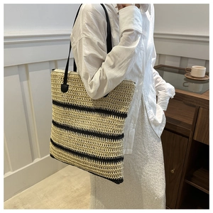 Detail of hand-woven straw bucket bag featuring nautical black stripes and slim shoulder straps