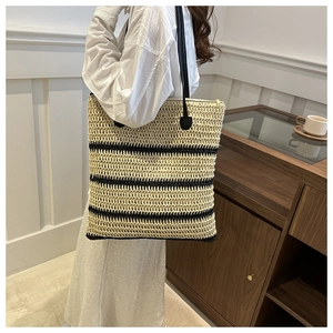 Detail of a large straw tote bag with black horizontal stripes and slim shoulder straps