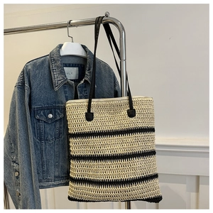 Détail d'un sac cabas en paille tressée à rayures noires suspendu à un rack
