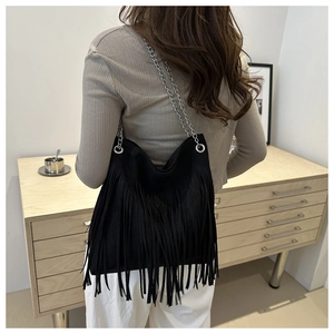Detail of black fringe tote bag with silver chain strap shown in a minimalist setting