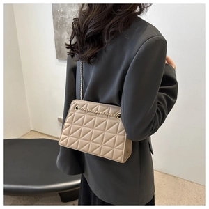 Detail of beige quilted crossbody bag with gold chain strap on model for summer fashion