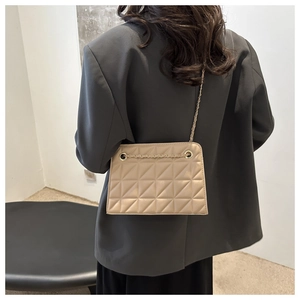 Detailed view of beige quilted crossbody bag with gold chain strap worn with grey suit