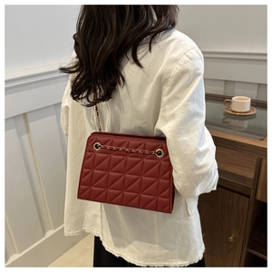 Detail of burgundy quilted crossbody bag with golden chain strap on a model shoulder